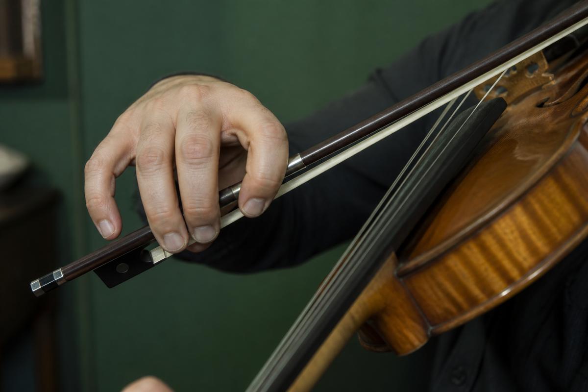 Adult right hand guiding a violin bow across the strings